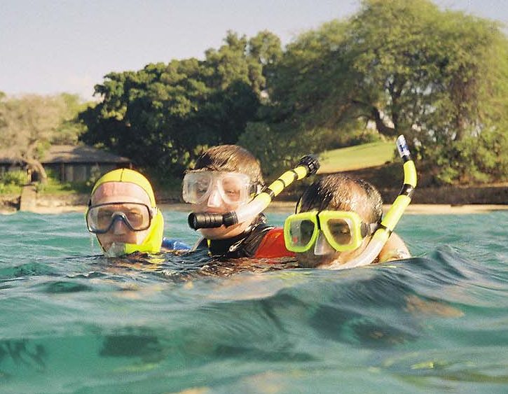 3 adults in full snorkeling gear, heads above water in the ocean, posing for a photo